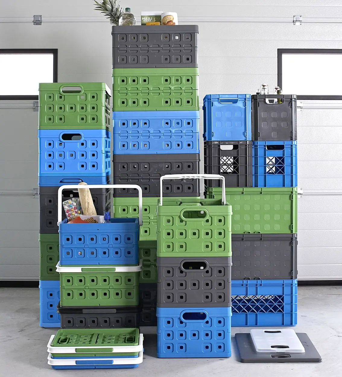 Stapel aus ca. 20 Kunststoff-Faltboxen, grün, blau und grau, einige mit weißen Henkelgriffen